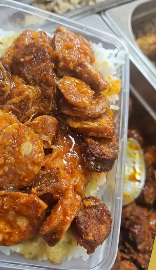 Une barquette de saucisses en sauce sur son riz, devant les bacs du comptoir